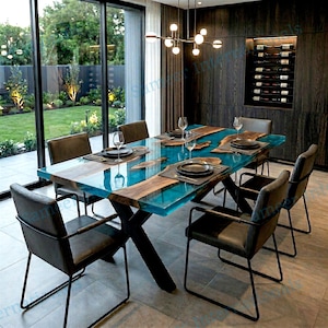 May include: A contemporary dining table featuring a turquoise resin centre and wooden borders. The table is set with black plates, placemats, and glassware. Black metal chairs surround the table. A wine rack is visible in the background.