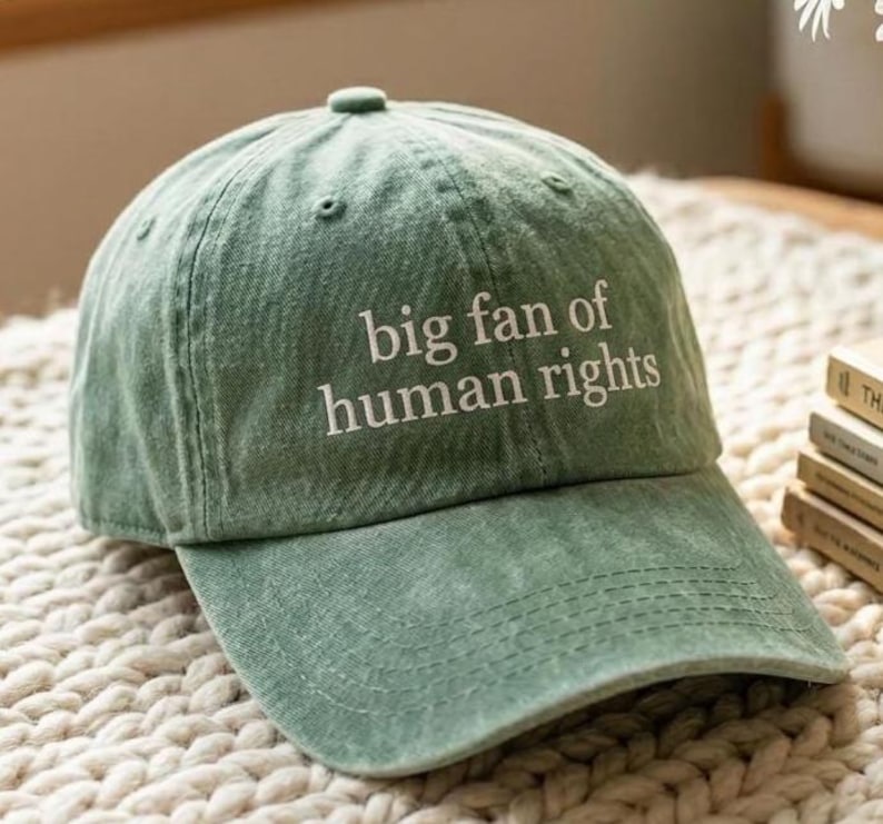 K&ouml;nnte beinhalten: Eine hellgr&uuml;ne Baseballkappe mit dem wei&szlig;en Schriftzug "big fan of human rights". Die Kappe hat einen gebogenen Schirm und einen Stoffriemenverschluss. Der Hut ist aus weichem, strukturiertem Material.