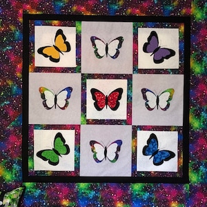 May include: A quilt with a black background and a galaxy print. The quilt is divided into nine squares, each with a different colored butterfly. The butterflies are red, blue, green, purple, and white.