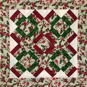 Könnte beinhalten: Ein quadratischer Quilt mit Weihnachtsmotiv. Das Quilt zeigt ein zentrales Design aus abwechselnd roten und grünen diagonalen Streifen mit weißen Dreiecken in den Ecken. Der Hintergrundstoff hat ein Muster aus Stechpalmenblättern und roten Beeren.