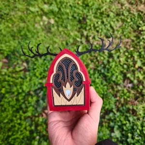May include: A red, brown, and beige decorative object with black antlers. The object has a window-like design with a mesh pattern and a light blue accent. The antlers extend from the top of the object.