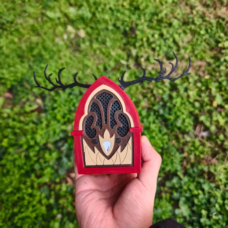 May include: A red, brown, and beige decorative object with black antlers. The object has a window-like design with a mesh pattern and a light blue accent. The antlers extend from the top of the object.