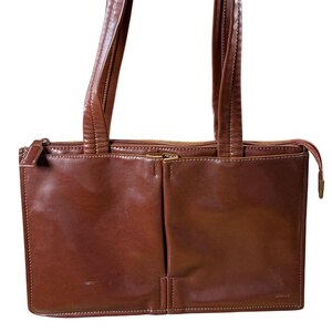 May include: A brown leather tote bag with two compartments and two handles. The bag has a zipper closure and a small zipper pocket on the front. The stitching is white, and the bag has a glossy finish.