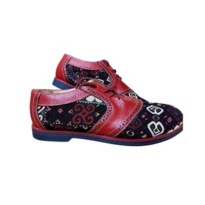 May include: A pair of lace-up oxford shoes featuring red pebbled leather overlays and black fabric panels embroidered with intricate, colorful geometric patterns. The shoes have a classic wingtip-style perforated trim and a solid dark sole.