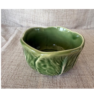Peut inclure: Un bol en céramique vert sauge brillant en forme de tête de chou. L'extérieur présente un motif de feuilles moulées et texturées avec des nervures en relief et un bord festonné irrégulier imitant l'aspect naturel des feuilles de chou.