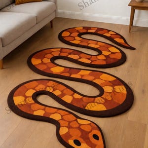 May include: Three snake-shaped rugs in shades of orange, brown, and yellow. The rugs are arranged on a light-coloured wooden floor. The rugs have a textured pattern and a dark brown border. The rugs are in a room with a sofa and side table.