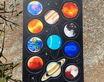 May include: A black sticker sheet featuring colorful illustrations of planets. Each planet is depicted in a circular design with detailed textures and colors, set against a starry background. The sheet includes planets like Earth, Mars, and Saturn.