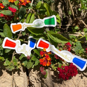 May include: Three colorful stickers featuring a pair of red, blue, and green cups connected by a string with the text "Communication" and "Call me" written in gold.