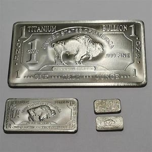 May include: A collection of titanium bullion bars and coins. The largest bar features a buffalo image and reads "United States of America" and "One Troy Ounce." Smaller bars and coins are also visible.