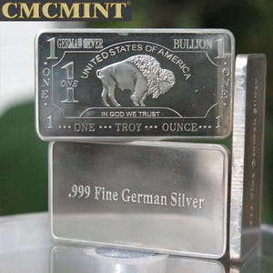 May include: Two rectangular German silver bullion bars. The top bar features a buffalo image and the text "UNITED STATES OF AMERICA" and "ONE TROY OUNCE." The bottom bar is stamped with ".999 Fine German Silver."