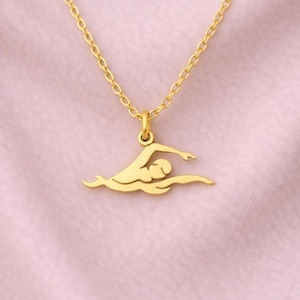 Peut inclure: Collier doré avec un pendentif nageur. Le pendentif représente un nageur en nage libre. La chaîne et le pendentif sont en or brillant. Le fond est de couleur rose clair.