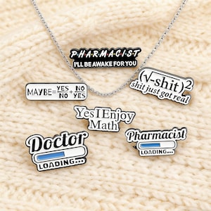 May include: A silver chain necklace with several enamel pins. The pins have various phrases, including "PHARMACIST I'LL BE AWAKE FOR YOU", "MAYBE=YES/NO", "(√-shit)2 shit just got real", "Yes I Enjoy Math", "Doctor LOADING...", and "Pharmacist LOADING...".