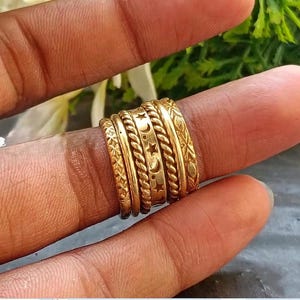 Op de afbeelding: Een set van vijf gestapelde goudkleurige metalen ringen. De ringen hebben verschillende texturen en patronen, waaronder een ster- en maanmotief, gedraaide touwontwerpen en ingewikkelde florale of geometrische gravures op de banden.