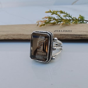 Op de afbeelding: Een zilveren ring met een grote, rechthoekige, gefacetteerde rookkwarts edelsteen. De ringband bestaat uit drie dunne, parallelle zilveren draden die samenkomen bij de zetting, geaccentueerd met kleine zilveren bolletjes. Tekst ZIVRAJEWELS.
