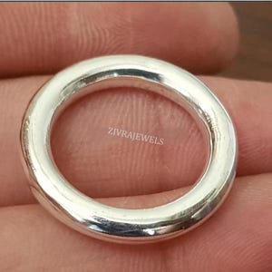 May include: A polished silver ring with a smooth, rounded band. The surface of the ring features the text ZIVRAJEWELS printed in a light colour. The ring has a simple, circular design with a reflective metallic finish and a consistent thickness.