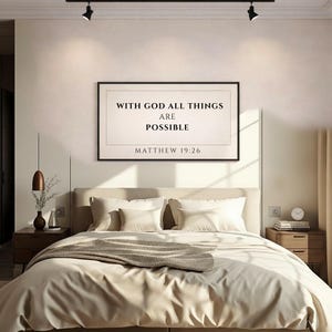 Puede incluir: Un dormitorio con una cama con ropa de cama y almohadas color crema. Un cuadro enmarcado en la pared muestra el texto "WITH GOD ALL THINGS ARE POSSIBLE" y "MATTHEW 19:26". La habitación está iluminada con luz suave.