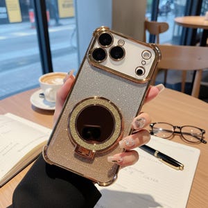 May include: A gold and silver glitter phone case with a ring holder. The case has a gold frame and a circular ring holder with a dark center. The phone case is held in a person's hand.