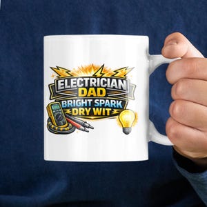 Może przedstawiać: Biały ceramiczny kubek z napisem "Electrician Dad Bright Spark Dry Wit" w kolorze czarnym, żółtym i pomarańczowym. Kubek przedstawia kreskówkowy obraz multimetru i żarówki.