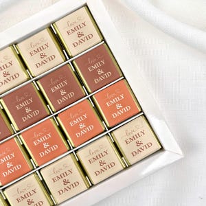 May include: A white box containing individually wrapped chocolates. Each chocolate is a different shade of brown and features the text "love EMILY & DAVID" in a cursive font. The chocolates are arranged in a grid.