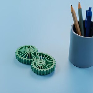 May include: A light blue cylindrical pencil holder with pencils and pens, next to two green gear-shaped objects. The pencils are brown and gray. The pens are blue and black. The background is light blue.
