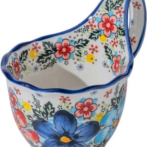 Könnte beinhalten: Weiße Keramikservierschale mit Henkel, verziert mit einem Blumenmuster in Rot, Blau und Gelb. Der Rand und der Henkel sind blau umrandet. Die Schale hat einen gewellten Rand.