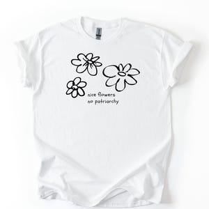 Könnte beinhalten: Weißes T-Shirt mit Rundhalsausschnitt und hochgekrempelten Ärmeln. Das Shirt zeigt ein schwarzes, handgezeichnetes Blumenmuster mit dem Text "nice flowers no patriarchy" in einer einfachen, handschriftlichen Schriftart. Das Shirt besteht aus einem weichen, leichten Material.