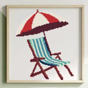 Op de afbeelding: Een ingelijst kruissteekkunstwerk toont een strandscène. Een gestreepte strandstoel met blauw-witte strepen staat onder een rood-wit gestreepte parasol. Het kunstwerk is ingelijst in een licht houten frame.