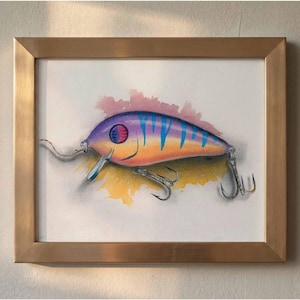 Pode incluir: Ilustração emoldurada de uma isca de pesca colorida. A isca é pintada com um gradiente de roxo, laranja e amarelo, acentuado com listras azuis. A obra de arte é emoldurada em uma moldura dourada.