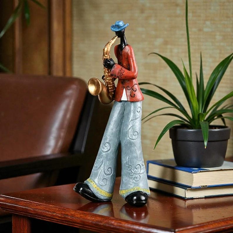 May include: A decorative figurine of a jazz musician playing a saxophone. The figure is dressed in a red jacket, blue trousers, and a blue hat. The saxophone is gold-coloured, and the figure has black skin.