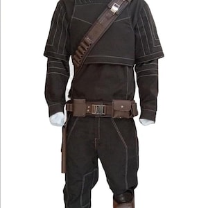 May include: Black costume with a high collar, shoulder strap, and belt with pouches. The outfit includes a long-sleeved top, trousers, and knee-high boots. White stitching details the seams. The costume is displayed on a mannequin.