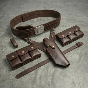 K&ouml;nnte beinhalten: Ein dunkelbraunes Leder-G&uuml;rtelset bestehend aus einem breiten Hauptg&uuml;rtel mit silberfarbener Metallschnalle, zwei separaten Drei-Taschen-Beuteln mit goldfarbenen Druckkn&ouml;pfen sowie einem strukturierten Holster mit passendem Druckknopf.