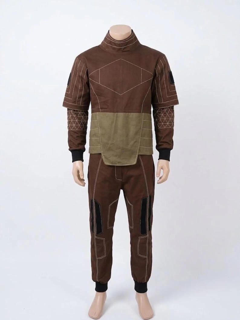 May include: A brown two-piece outfit on a mannequin. The top has a high collar and geometric stitching. The midsection is olive green. The pants have black accents on the knees and black cuffs. The outfit is designed with a futuristic aesthetic.