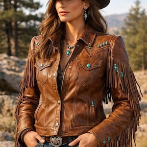 May include: A brown leather jacket featuring long fringe detailing on the sleeves and chest, accented with small turquoise stones. The jacket includes a collared neckline, button-down front, two chest pockets, and long sleeves with fringe.