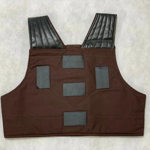 Puede incluir: Un chaleco marr&oacute;n con hombreras de cuero negro y parches rectangulares grises. El chaleco est&aacute; hecho de una tela duradera y tiene un dise&ntilde;o de cuello en V. Las hombreras est&aacute;n acolchadas.