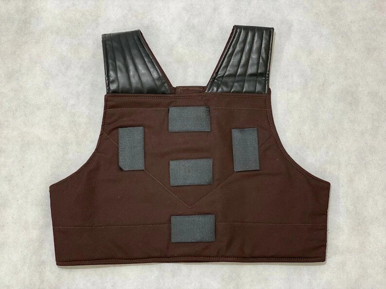 Puede incluir: Un chaleco marr&oacute;n con hombreras de cuero negro y parches rectangulares grises. El chaleco est&aacute; hecho de una tela duradera y tiene un dise&ntilde;o de cuello en V. Las hombreras est&aacute;n acolchadas.