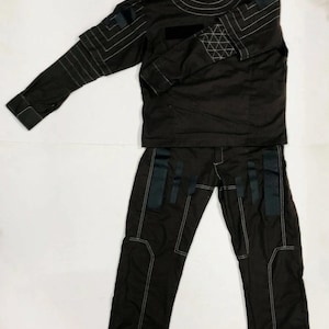 Puede incluir: Un conjunto de uniforme t&aacute;ctico marr&oacute;n oscuro, que incluye una parte superior de manga larga con cuello alto y pantalones a juego. La parte superior y los pantalones presentan costuras blancas y detalles en negro. El uniforme est&aacute; dise&ntilde;ado con una est&eacute;tica moderna y utilitaria.