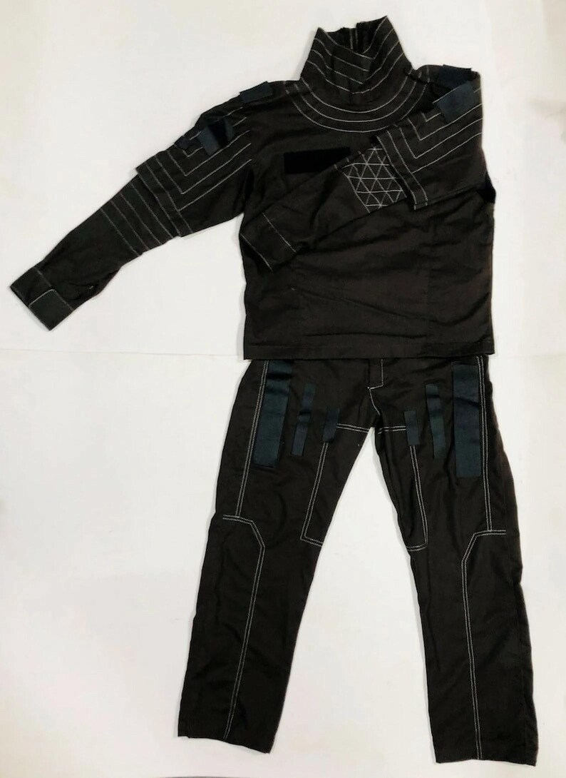 Puede incluir: Un conjunto de uniforme t&aacute;ctico marr&oacute;n oscuro, que incluye una parte superior de manga larga con cuello alto y pantalones a juego. La parte superior y los pantalones presentan costuras blancas y detalles en negro. El uniforme est&aacute; dise&ntilde;ado con una est&eacute;tica moderna y utilitaria.