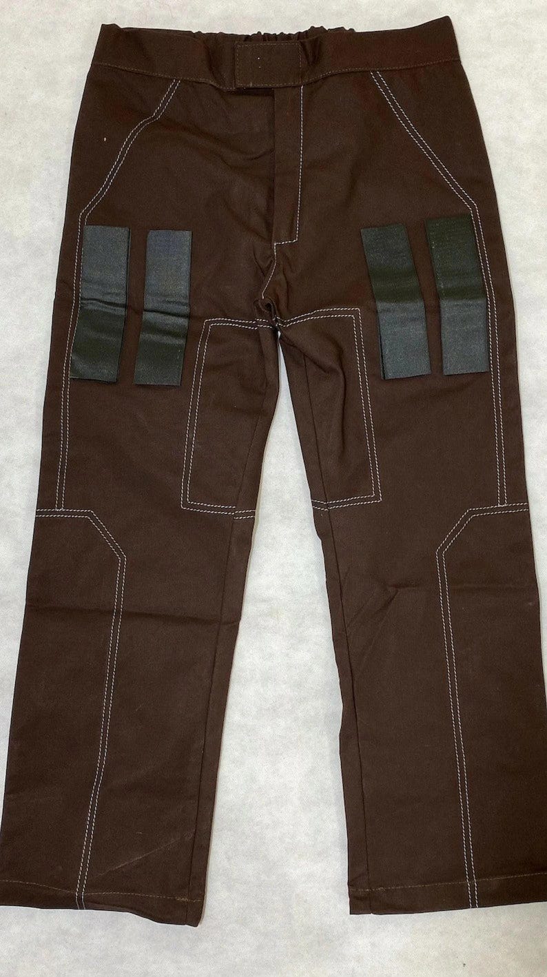 Puede incluir: Pantalones marrones con costuras blancas y parches rectangulares negros. Los pantalones tienen un dise&ntilde;o cl&aacute;sico con cierre de bot&oacute;n y cremallera. Los detalles de costura a&ntilde;aden un toque &uacute;nico.