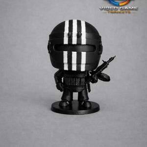 May include: A black figurine of a character from a video game, with a black helmet featuring three white stripes. The figure is holding a black weapon and stands on a black base. The logo "VGT VIDEO GAME TRINKETS" is in the background.
