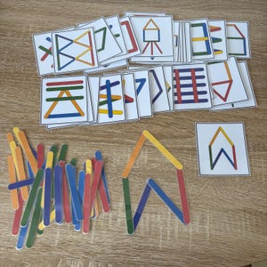 Può includere: Una collezione di giocattoli educativi, tra cui bastoncini di ghiacciolo colorati e carte abbinate. Le carte presentano forme e motivi geometrici. I bastoncini sono di vari colori e alcuni sono disposti a formare una casa.