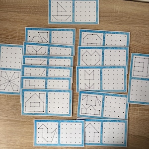 Può includere: Una collezione di carte bianche con bordi blu, ciascuna con una griglia di punti e un disegno a tratto nero. I disegni raffigurano varie forme, tra cui una barca, una casa e un cuore. Le carte sono disposte su una superficie di legno.