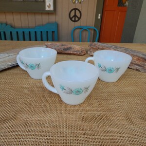 K&ouml;nnte beinhalten: Drei wei&szlig;e Keramik-Teetassen mit einem blauen Blumendesign. Die Tassen haben eine matte Oberfl&auml;che und sind mit einem zarten Muster aus blauen Blumen und gr&uuml;nen Bl&auml;ttern verziert.