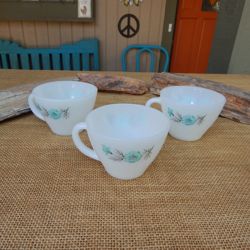 K&ouml;nnte beinhalten: Drei wei&szlig;e Keramik-Teetassen mit einem blauen Blumendesign. Die Tassen haben eine matte Oberfl&auml;che und sind mit einem zarten Muster aus blauen Blumen und gr&uuml;nen Bl&auml;ttern verziert.