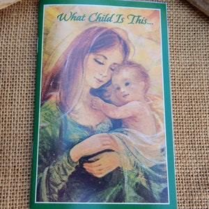 May include: A vintage Christmas card featuring a painting of Mary holding baby Jesus. The card has a green border and the text "What Child Is This..." at the top.