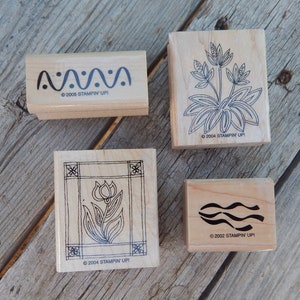 Peut inclure: Quatre tampons en caoutchouc en bois avec des motifs d'encre noire. Les tampons pr&eacute;sentent une ligne ondul&eacute;e, une fleur dans un cadre, une fleur avec des feuilles et une ligne ondul&eacute;e avec des points.