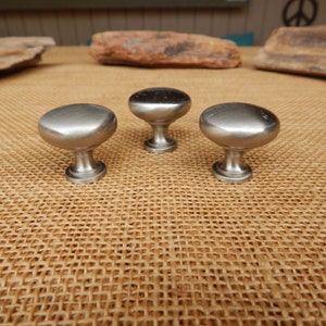 May include: Three silver cabinet knobs with a round, slightly domed top and a short, cylindrical base.