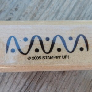 Peut inclure: Un tampon en bois avec un motif de ligne ondul&eacute;e et des points noirs. Le texte "&copy; 2005 STAMPIN' UPI" est imprim&eacute; sur le tampon.