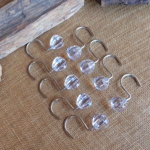 May include: Ten clear plastic shower curtain hooks with a silver metal hook. The hooks have a faceted design.