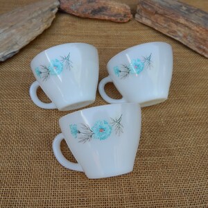 K&ouml;nnte beinhalten: Drei wei&szlig;e Keramikbecher mit blauen Blumendesigns. Die Becher haben eine abgerundete Form und einen Henkel an der Seite.