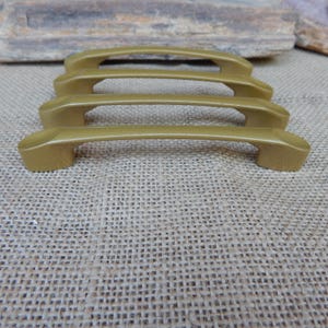 May include: Four gold-colored cabinet pulls arranged in a row. Each handle features a smooth, arched design with a solid, matte finish and two mounting points at the ends. The hardware is uniform in shape and color, showcasing a simple, functional aesthetic for furniture or cabinetry applications.